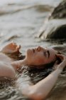Mujer joven yace en el agua con los ojos cerrados - foto de stock