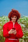 Cara jovem com cabelo encaracolado vermelho na década de 80 terno esportivo vermelho e telefone celular no exterior — Fotografia de Stock
