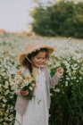 Una niña está de pie en un campo con un ramo de margaritas - foto de stock