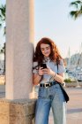 Junge rothaarige Frau blickt in einer Hafenstadt auf ihr Handy — Stockfoto