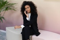 Чорна ділова жінка в формальному одязі сидить в офісі і розмовляє по телефону . — стокове фото