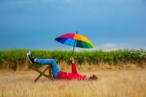 Cara com um guarda-chuva senta-se em uma cadeira deitada no chão no campo — Fotografia de Stock