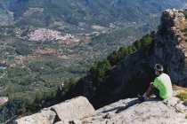 Seitenansicht eines Mannes, der auf einer Klippe sitzt und auf die Berge blickt — Stockfoto