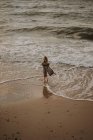 Chica con el pelo rubio en una gabardina caminando por el mar - foto de stock