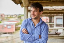 Young Caucasian man with his arms crossed smiling on the terrace of his hut. — Stock Photo