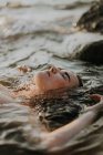 Jeune femme gît dans l'eau les yeux fermés — Photo de stock