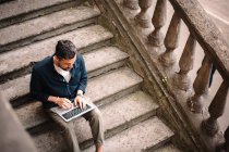 Человек с ноутбуком сидит на ступеньках в городе — стоковое фото