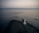 Drohnenblick auf den weißen Leuchtturm an der Felsküste in der Nähe der wogenden See an einem stürmischen Morgen in Island — Stockfoto