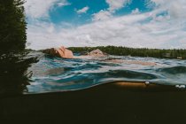 Vista dividida del niño flotando en un lago en un cálido día de verano. - foto de stock