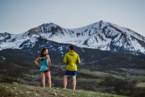 Dois amigos recuperam o fôlego enquanto correm na frente de um grande pico — Fotografia de Stock