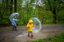 Niño y niña jugando bajo la lluvia con sombrillas - foto de stock