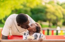 Padre besando a su hija pequeña en los juegos del parque - foto de stock