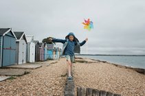 Junge balanciert am Strand auf einer Mauer und spielt mit einer Windmühle — Stockfoto