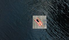 Aerial of woman relaxing alone on floating dock on lake in summer. — Stock Photo