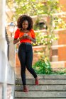 Bela fotografia de uma jovem mulher africana andando e enviando uma mensagem de seu smartphone — Fotografia de Stock
