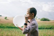 Smartly dressed boy blowing up a balloon at a wedding in summer — Stock Photo