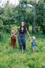 Una giovane madre e i suoi figli camminano nell'erba alta nel frutteto — Foto stock