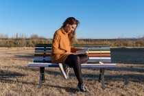 Латинская девушка читает книгу о многоцветной скамейке — стоковое фото