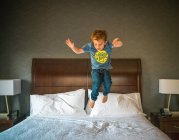 Petit garçon sautant sur le lit dans la chambre — Photo de stock