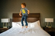 Menino pulando na cama no quarto — Fotografia de Stock