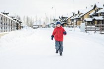 El chico se divierte caminando en el abrigo rojo en el pueblo de invierno. - foto de stock