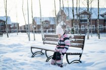 A linda garota sentada em um banco na aldeia de inverno. — Fotografia de Stock