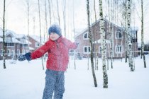 El chico se divierte caminando en el abrigo rojo en el pueblo de invierno. - foto de stock