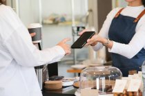 Customer making payment using NFS technology at coffee cafe. Small business owner and contactless or wireless payment concept — Stock Photo