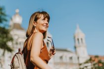Young beautiful woman with long hair in a white dress and a backpack on the roof of the city — Stock Photo