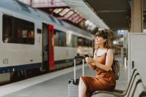 Молода жінка з рюкзаком сидить на залізничній платформі — стокове фото