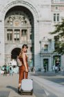 Молода жінка з валізою, що йде на вулиці — стокове фото