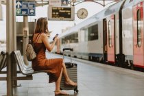 Молода жінка з рюкзаком сидить на лавці на залізничному вокзалі — стокове фото