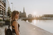 Молодая женщина с длинными волосами в черном платье и рюкзаком на мосту — стоковое фото
