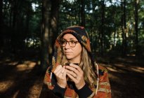 Jovem mulher em um chapéu e óculos com uma mochila na floresta — Fotografia de Stock
