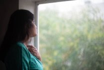 Jovem mulher vestindo vestido verde olhando para fora através da janela — Fotografia de Stock