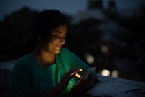 Молода жінка дивиться мобільний на даху в блакитну годину — стокове фото