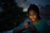 Jeune femme regardant mobile sur le toit en heure bleue — Photo de stock