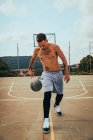 Joven chico latino tatuado jugando con una pelota de baloncesto en una cancha - foto de stock