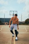 Giovane ragazzo latino tatuato che gioca con una pallacanestro su un campo — Foto stock