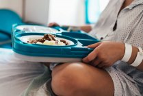 Young woman hospitalized in a bed. Holding hospital food tray. Side view. — Stock Photo
