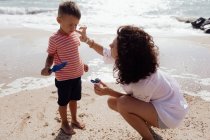 Cuidar mamá unta crema solar en su hijo en la orilla del mar - foto de stock
