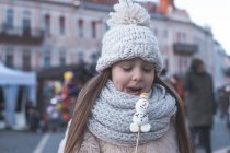 Outdoor portrait of little girl at the Christmas fair eating marshmallow snowman — Stock Photo