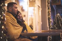 Casal romântico sentado no sofá no café ao ar livre durante o tempo de Natal — Fotografia de Stock