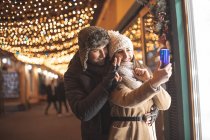 Romantisches Paar spaziert und telefoniert per Video zu Verwandten in der Stadt mit Weihnachtsdekoration — Stockfoto