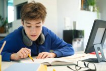 Enseignement à distance en ligne. Un écolier étudie à la maison et fait ses devoirs à l'école. Un enseignement à distance à domicile. — Photo de stock