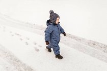 Маленький мальчик в синих ползунках уверенно гуляет по снегу — стоковое фото