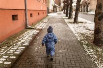 Kleiner Junge in blauem Hemd und Wintermütze läuft auf Gehweg — Stockfoto