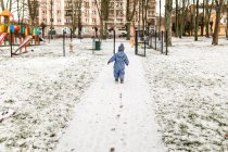 Маленький мальчик в синих ползунках и теплая шляпа идут на детскую площадку — стоковое фото