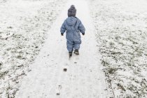 Petit garçon en bleu onesie et chapeau chaud marchant sur une neige — Photo de stock