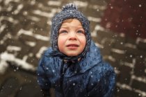 Kleiner Junge in blauer Winterkleidung blickt in den verschneiten Himmel — Stockfoto